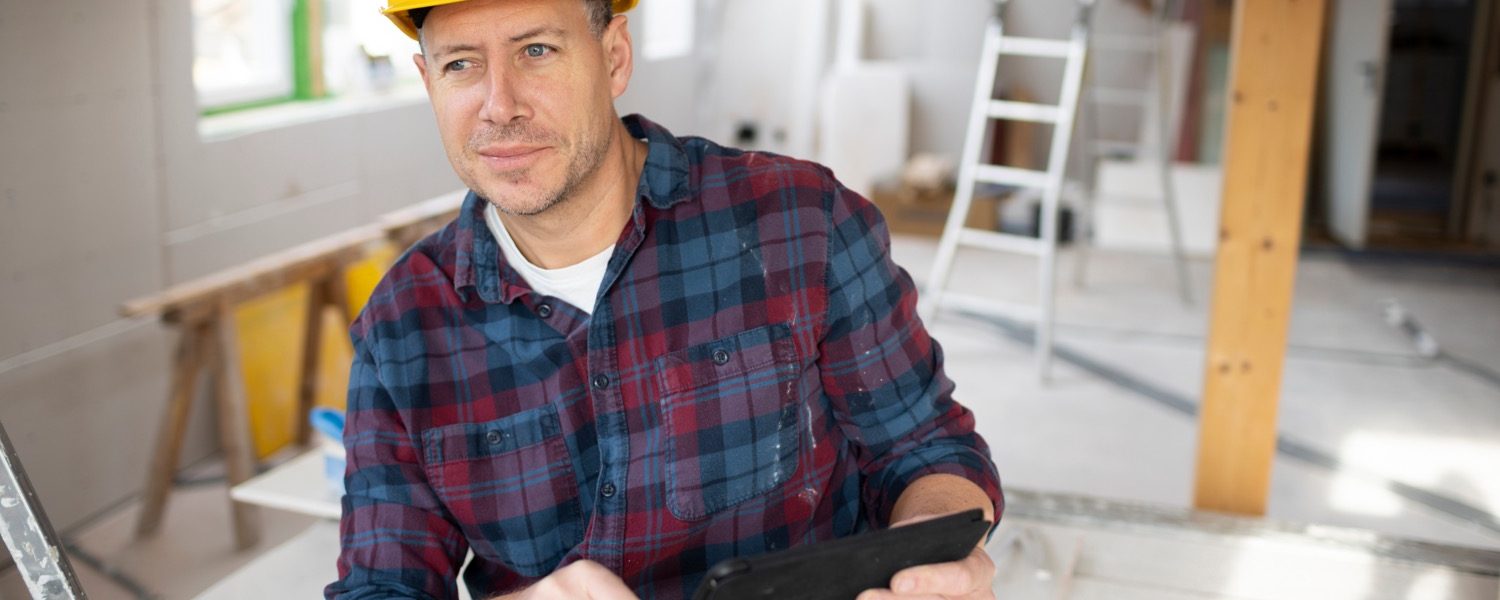 middle aged man on building site with yellow helmet and checkered shirt working with his tablet